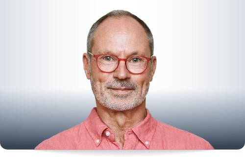 Ein 56 jahre alter Mann mit Dreitagebart, roter Brille und einem roten Leinenhemd.